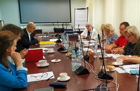 Pokaż zdjęcie: Grupa osób siedzących naprzeciw sobie przy dużym prostokątnym stole w sali konferencyjnej 