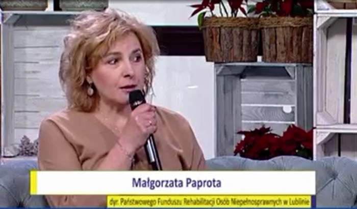 Pokaż zdjęcie: Kobieta trzyma w ręku mikron. W tle czerwone kwiaty w bezowych osłonkach