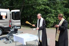 Pokaż zdjęcie: Dwóch księży stoi przed nowym autem.Jeden s księży trzyma kropidło a drugi mikrofon