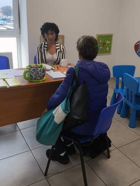 Pokaż zdjęcie: Przy biurku rozmawiają kobieta z mężczyzną, na stole leżą ulotki.