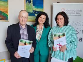 Pokaż zdjęcie: Laureaci kobieta i mężczyzna pozują do zdjęcia z panią dyrektor. W tle logo PFRON z 