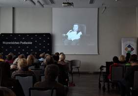 Pokaż zdjęcie: Zdjęcie zrobione z końca Sali, widać uczestników Konwentu, na ścianie kadr przedstawiający Annę Drabarz.