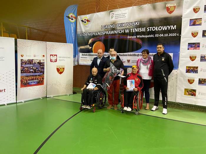 Pokaż zdjęcie: Zawodnicy na wózkach inwalidzkich z nagrodami na tle baneru Grand Prix
