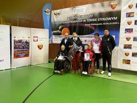 Pokaż zdjęcie: Zawodnicy na wózkach inwalidzkich z nagrodami na tle baneru Grand Prix