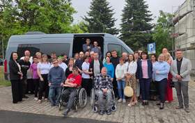 Duża grupa osób stoi na tle busa. Pośród tych osób osoby na wózkach inwalidzkich.