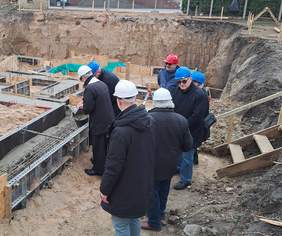 Pokaż zdjęcie: 7 osób z kaskach dokonuje wmurowania aktu erekcyjnego na placu budowy