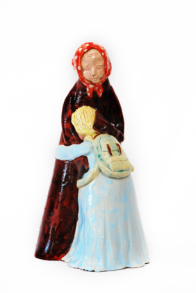 Pokaż zdjęcie: Rzeźba przedstawiająca dwie wtulone w siebie osoby, babcie i wnuczkę. Babcia ubrana w długa ciemną spódnicę i chustę na głowie przytula dziewczynkę, blondynkę ubraną w niebieską sukienkę i żółty plecak, wtulona w babcię. Dziewczynka jest mała sięga babci do ramienia.