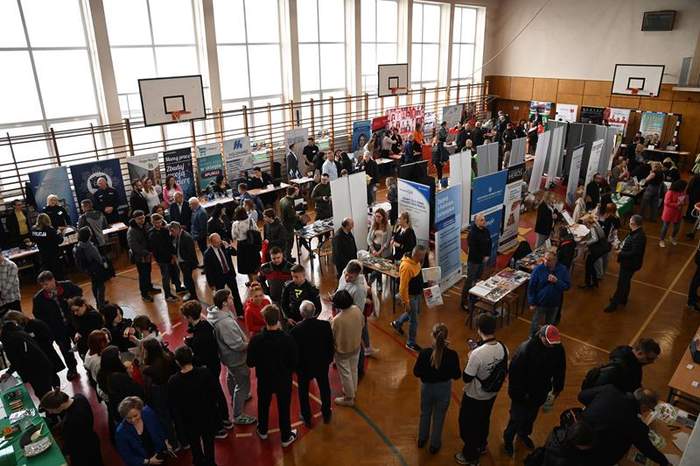 Pokaż zdjęcie: Zdjęcie z balkonu na salę gimnastyczną na której odbywały się targi pracy. Przy stoiskach jest dużo zainteresowanych osób.