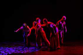 Pokaż zdjęcie: Scena, na której tańczy 5 osób ubranych w ciemne stroje.