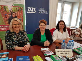 trzy kobiety przy stole, siedzą patrzą w obiektyw, uśmiechają się