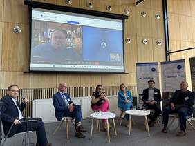 Pokaż zdjęcie: Zdjęcie uczestników panelu dyskusyjnego siedzących na krzesełkach.