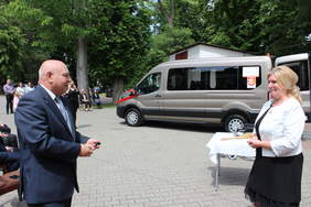 Pokaż zdjęcie: Mężczyzna trzyma kluczyki,które wręczy kobiecie na tle nowego busa