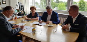 Osoby podpisujące umowę, siedzący przy stole, 3 mężczyzn i 1 kobieta, osoby uśmiechają się