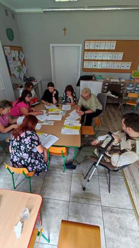 Pokaż zdjęcie: Uczestnicy warsztatów w kameralnej sali szkolnej pracują w grupie.
