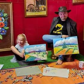 Pokaż zdjęcie: Stanisław Kmiecik i Martynka Gruca prezentują prace, które stworzyli podczas obchodów III Dnia Artystów Malujących ustami i stopami