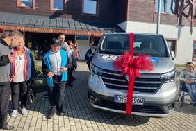 Pokaż zdjęcie: Przekazanie pojazdu dla uczestników ŚDS w Krynicy-Zdroju. Uśmiechnięci uczestnicy spotkania stoją obok samochodu