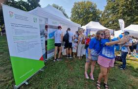 Pokaż zdjęcie: Tłum osób stoi przy stoisku informacyjnym PFRON. Oglądają materiały, rozmawiają z pracownikami Oddziału, niektórzy robią sobie zdjęcia.