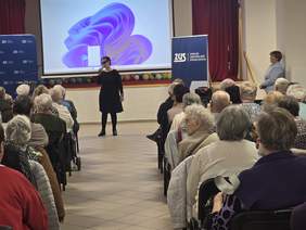 Kobieta ubrana na czarno, w ciemnych okularach, stoi z mikrofonem w ręku