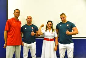 Pokaż zdjęcie: Dwóch mężczyzn w białych spodniach i zielonych koszulkach, jeden mężczyzna w czerwonej koszulce i jasnych spodniach, kobieta w białej sukience