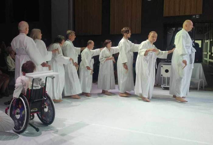 Pokaż zdjęcie: Na scenie widzimy aktorów ubranych w białe szaty stojących jeden za drugim