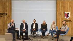Pokaż zdjęcie: Na środku sali siedzi 6 osób, prelegencci , prowadzacy IV panel Forum pn. "Zatrudnienie osoby z niepełnosprawnością intelektualną", w tle widać logo województwa kujawsko-pomorskiego oraz ROPS-u