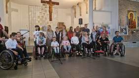 Pokaż zdjęcie: Na tle ołtarz stoi grupa młodzieży przed nimi na wózkach inwalidzkich siedzą dziewczęta i chłopcy.