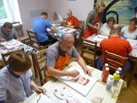 Pokaż zdjęcie: Uczestnicy ŚDS Caritas podczas zajęć plastycznych - dorosłe osoby z niepełnosprawnościami malują farbami portrety