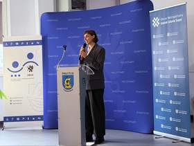 Kobieta przemawia przy mównicy z herbem Powiatu Puckiego, trzyma mikrofon. W tle niebieska ścianka z napisem „Powiat Pucki” oraz roll-upy dotyczące Roku Wsparcia Osób z Niepełnosprawnościami w Powiecie Puckim 2026.