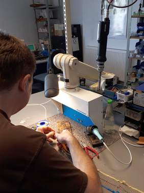 Pokaż zdjęcie: Monter elektronik w trakcie pracy,  na stoliku stoi specjalistyczna maszyna