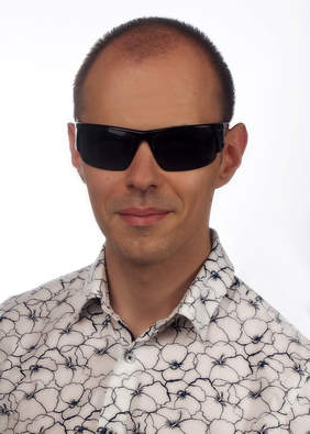 Pokaż zdjęcie: Na zdjęciu Szymon Wasiłowicz - portret młodego uśmiechniętego mężczyzny w czarnych okularach i białej koszuli