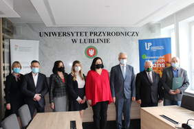 Pokaż zdjęcie: W sali konferencyjnej stoja czterej mężczyźni i cztery kobiety.W tle loga Uniwersyetu Przyrodniczego oraz PFRON