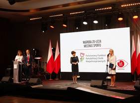 Pokaż zdjęcie: Prowadząca Galę zapowiada na scenie wręczenie PFRONowi nagrody Mecenasa Sportu, Prezes Maląg stoi obok na scenie