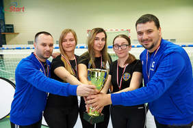 Pokaż zdjęcie: Pięć niedowidzących lub niewidomych osób w sportowych strojach - trzy kobiety i dwóch mężczyzn. Przed sobą trzymają złoty puchar. Wszyscy są uśmiechnięci.