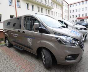Pokaż zdjęcie: zaparkowany srebrny bus marki Ford pod budynkiem, na masce samochodu logo osoby na wózku, na drzwiach samochodu napis Dom Pomocy Społecznej w Choroszczy.
