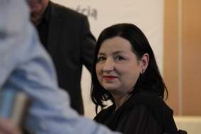 Pokaż zdjęcie: Zbliżenie na twarz kobiety z czarnymi włosami do ramion w średnim wieku. Kobieta lekko się uśmiecha i patrzy w obiektyw