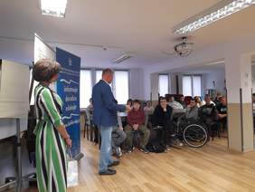 Pokaż zdjęcie: Mężczyzna w garniturze prowadzi wykład, zwrócony jest w stronę młodzieży.