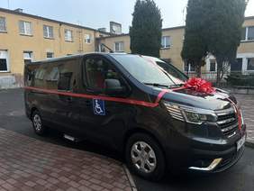 Pokaż zdjęcie: Mikrobus w kolorze czarnym, który jest owinięty czerwoną wstęgą