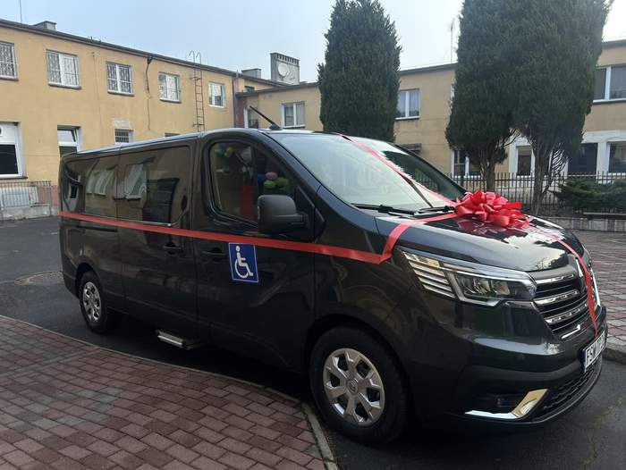 Pokaż zdjęcie: Mikrobus w kolorze czarnym, który jest owinięty czerwoną wstęgą