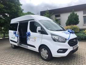 Pokaż zdjęcie: Mikrobus dla osób niepełnosprawnych w kolorze białym z otwartymi drrzwiami na podwórku