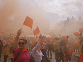 tłum ludzi w pomarańczowym dymie, machają, uśmiechają się