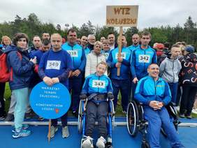 Pokaż zdjęcie: Na stadionie znajduje się drużyna Warsztatu Terapii Zajęciowej z Koluszek. Zawodnicy są ubrani na niebisko. Trzymają transparent swojej drużyny. 