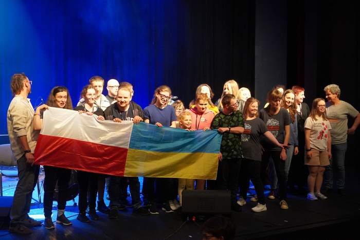 Pokaż zdjęcie: Na scenie stoi grupa aktorów do pamiątkowego zdjęcia, przed sobą trzymają flagę Polski i Ukrainy