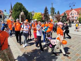 Pokaż zdjęcie: Ulicami Myślenic maszerują osoby z niepełnosprawnościami oraz oraz ich rodziny i opiekunowie. Wszyscy są ubrani na pomarańczowo.