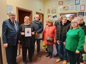 Pokaż zdjęcie: W Łódzkim Oddziale PFRON stoi grupa osób. Jedna pani prezentuje otrzymany dyplom. Z lewej strony stoi dyrektor Łódzkiego Oddziału PFRON. 