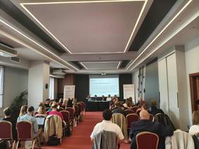 Sala konferencyjna, grupa siedzących osób, w tle prezentacja