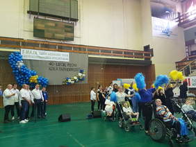 występ artystyczny, z lewej strony grupa osób śpiewa z prawej osób tańczy w tym osoby na wózkach inwalidzkich