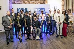 Pokaż zdjęcie: Na zdjęciu znajdują się nagrodzone osoby, które trzymają w rękach puchary. Stoją na tle grafiki Dziennika Elbląskiego