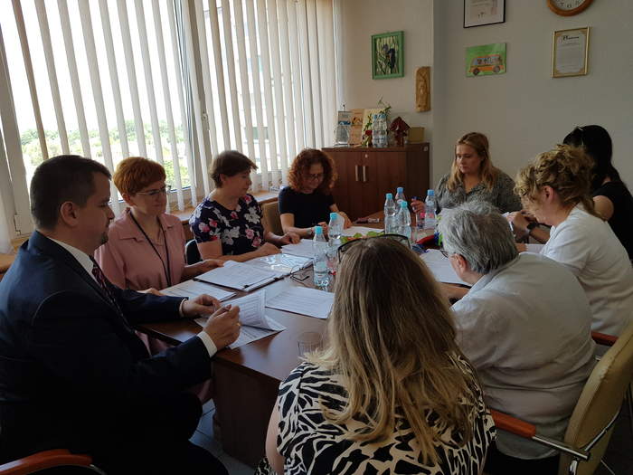 Pokaż zdjęcie: Osoby podpisujące umowę siedzą przy stole i parafują umowy