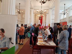 uczestnicy wydarzenia, poruszają się po dużej sali z kolumnami w urzędzie wojewódzkim.