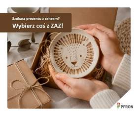 Kobiece dłonie trzymają odpakowany prezent. W tle widać pudełko prezentowe. Upominkiem jest talerz z narysowaną lwią głową. 